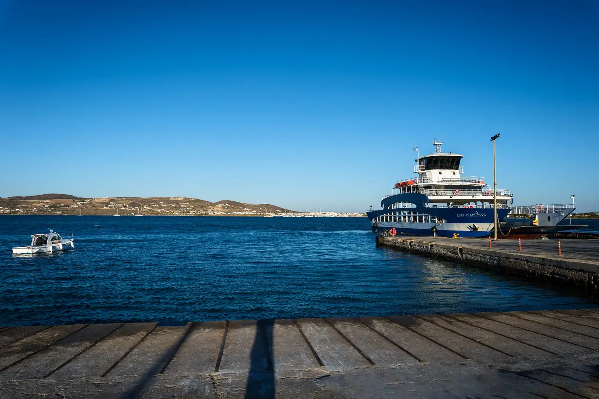 A ferry moored at a long pier, a small boat in the blue water and the coast beyond