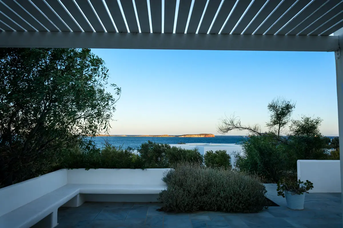 A white terrace with a built-in bench and shrubs, looking out over the sea to a small island