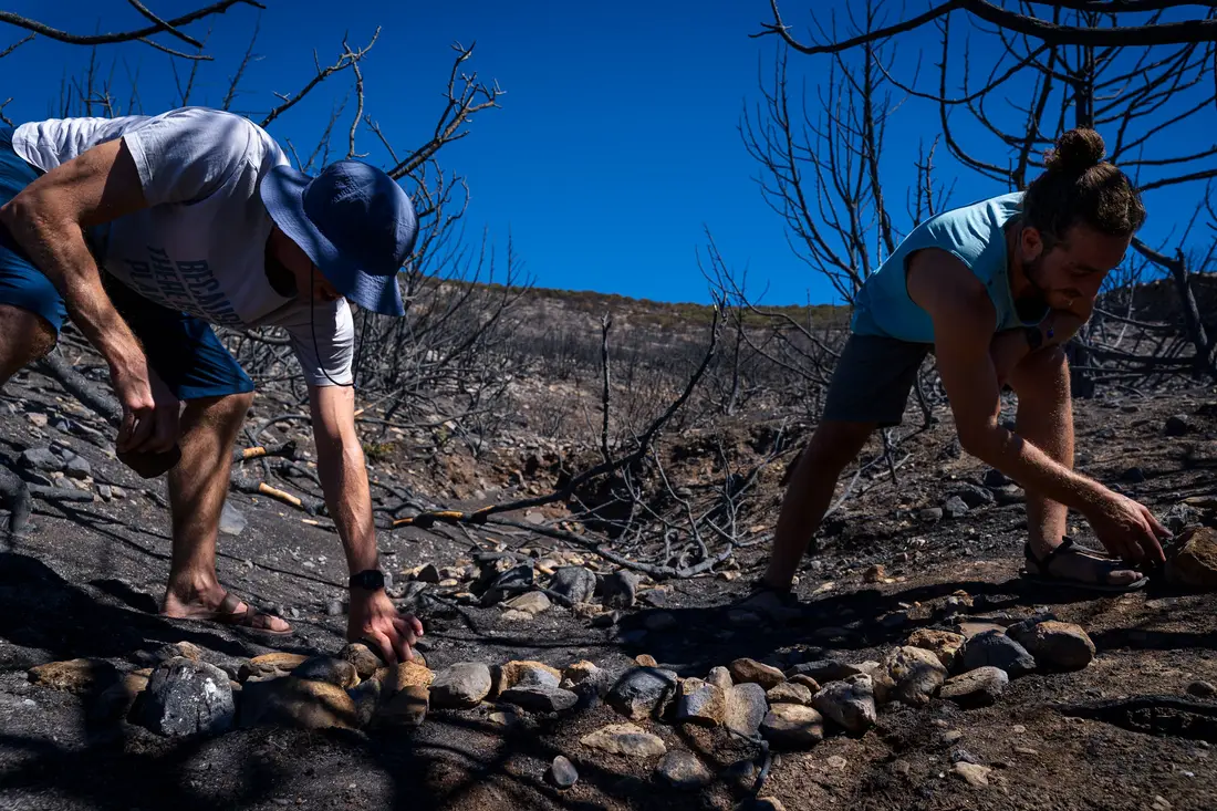 Two men bending to lay a line of stones on burnt ground under a blue sky