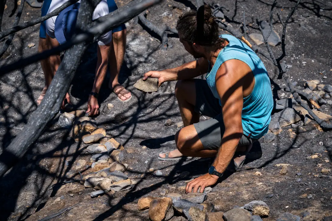 A man in a turquoise vest crouching to set stones into a line on scorched ground