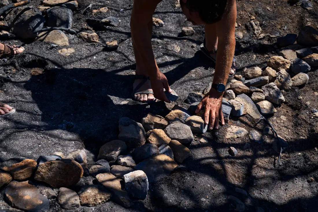 Hands setting stones into a curved line on dark burnt soil