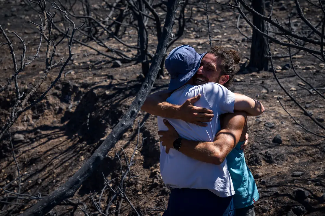 Two men hugging among burnt branches on a scorched hillside