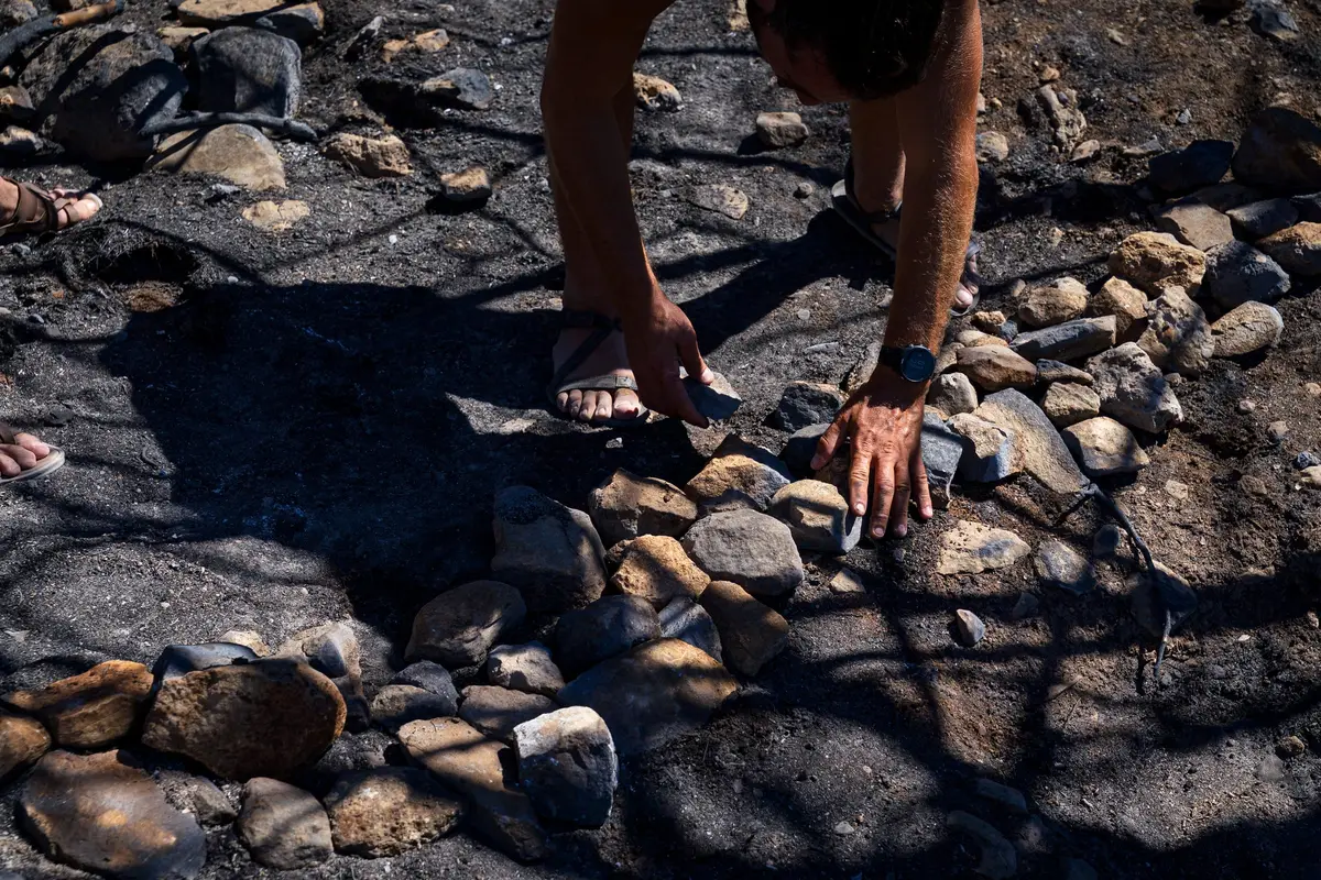 Hands laying stones in a row on burnt, ash-grey ground