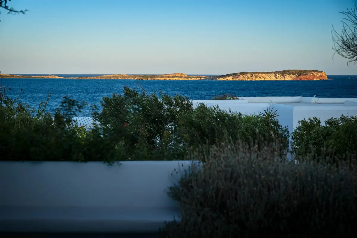 Calm blue sea and low islets seen over green shrubs and a white wall